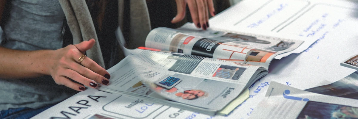 Realizziamo per te brochure e volantini Una donna al tavolo di lavoro sfoglia una brochure. Realizziamo per te brochure e volantini