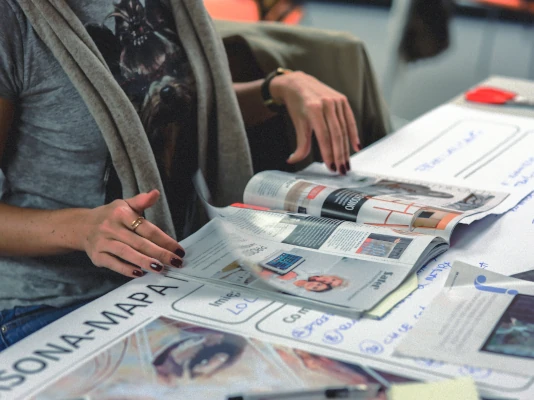 Realizziamo per te brochure e volantini Una donna al tavolo di lavoro sfoglia una brochure. Realizziamo per te brochure e volantini