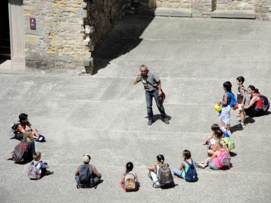 I nostri corsi sono la trasmissione del saper fare Uomo in piedi in mezzo a un semicerchio di ragazzi seduti che lo ascoltano. I nostri corsi sono la trasmissione del saper fare