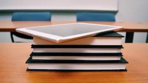 Quattro libri rilegati posati su un banco scolastico. Sopra di essi, un tablet. Realizziamo la manualistica che ti occorre, sia per la carta sia per il digitale
